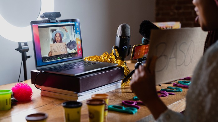 Gahmya’s Desk Is Filled With PlayDoh, Pom Poms, And Other Props As She Excitedly Records Herself On Her Laptop. | Digital Learning